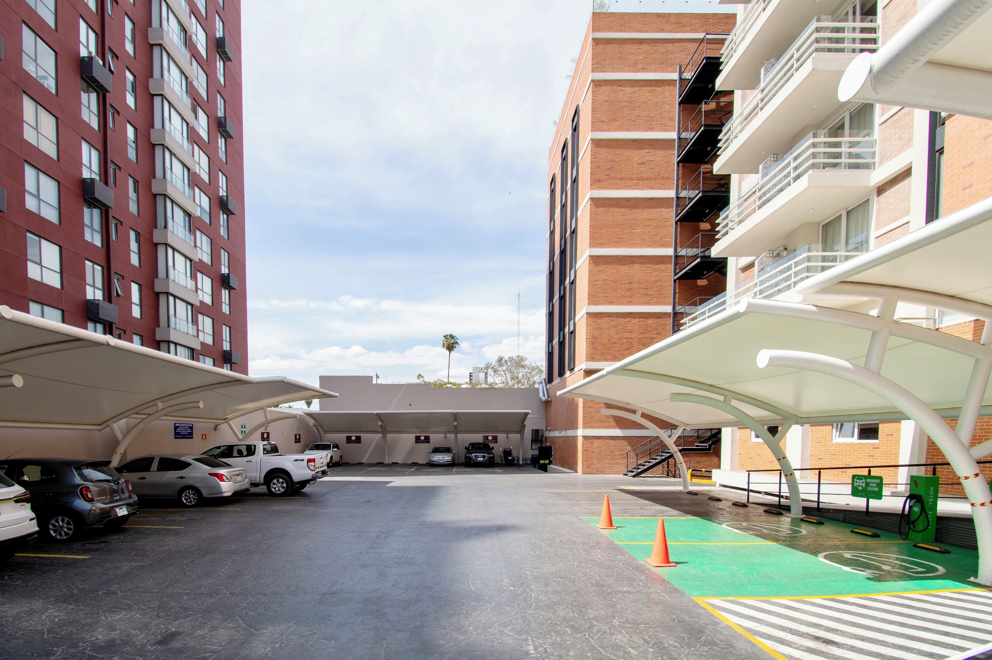 A parking area with multiple cars, a covered bike station, and a building with brick and glass facades.