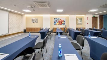 Un salón de conferencias con largas mesas, sillas y botellas de agua.