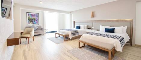 A modern hotel room with two beds, a sofa, a desk, and a large window.