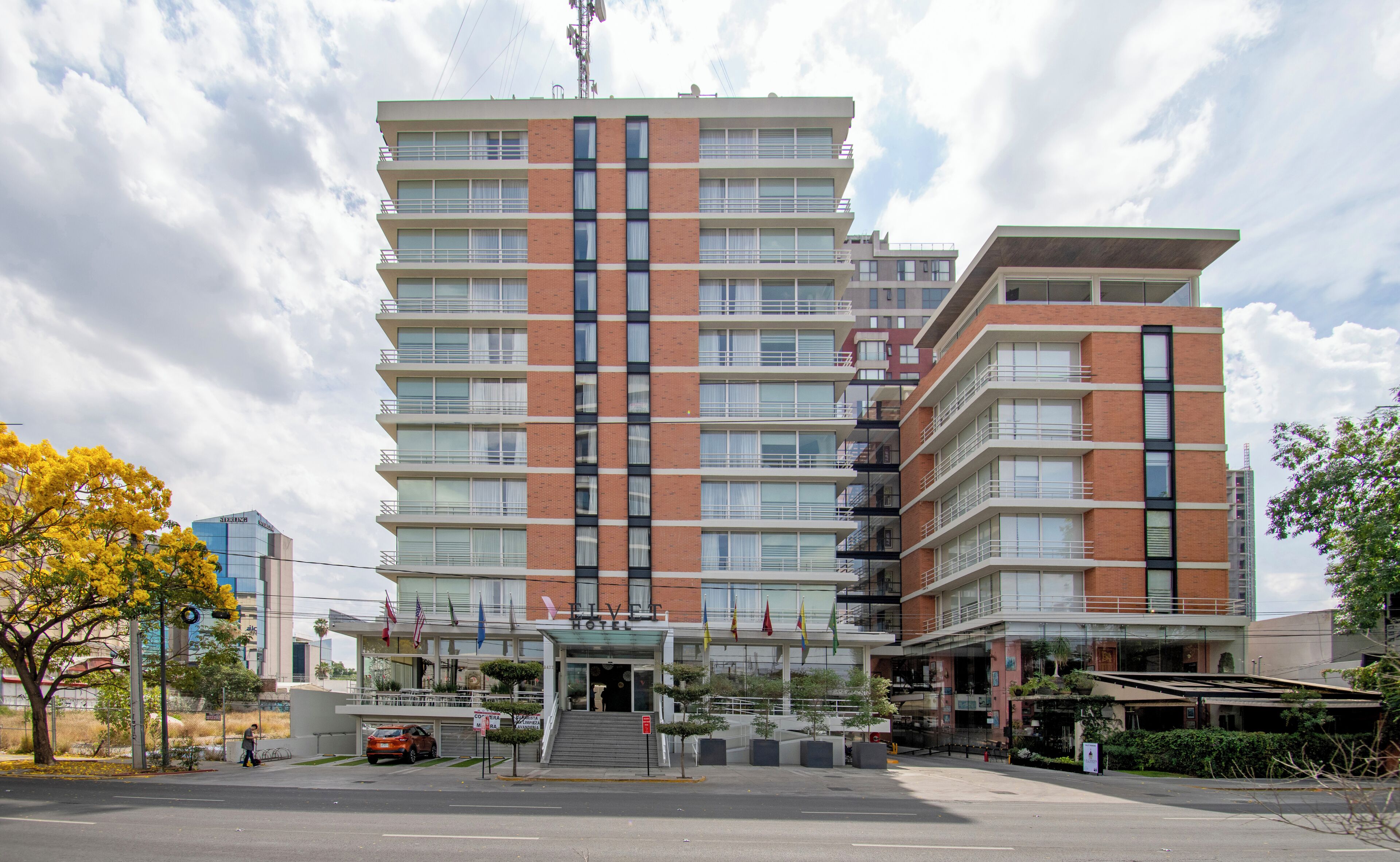 A multi-story hotel with a modern design, featuring a prominent entrance with steps, a glass facade, and a flat roof.