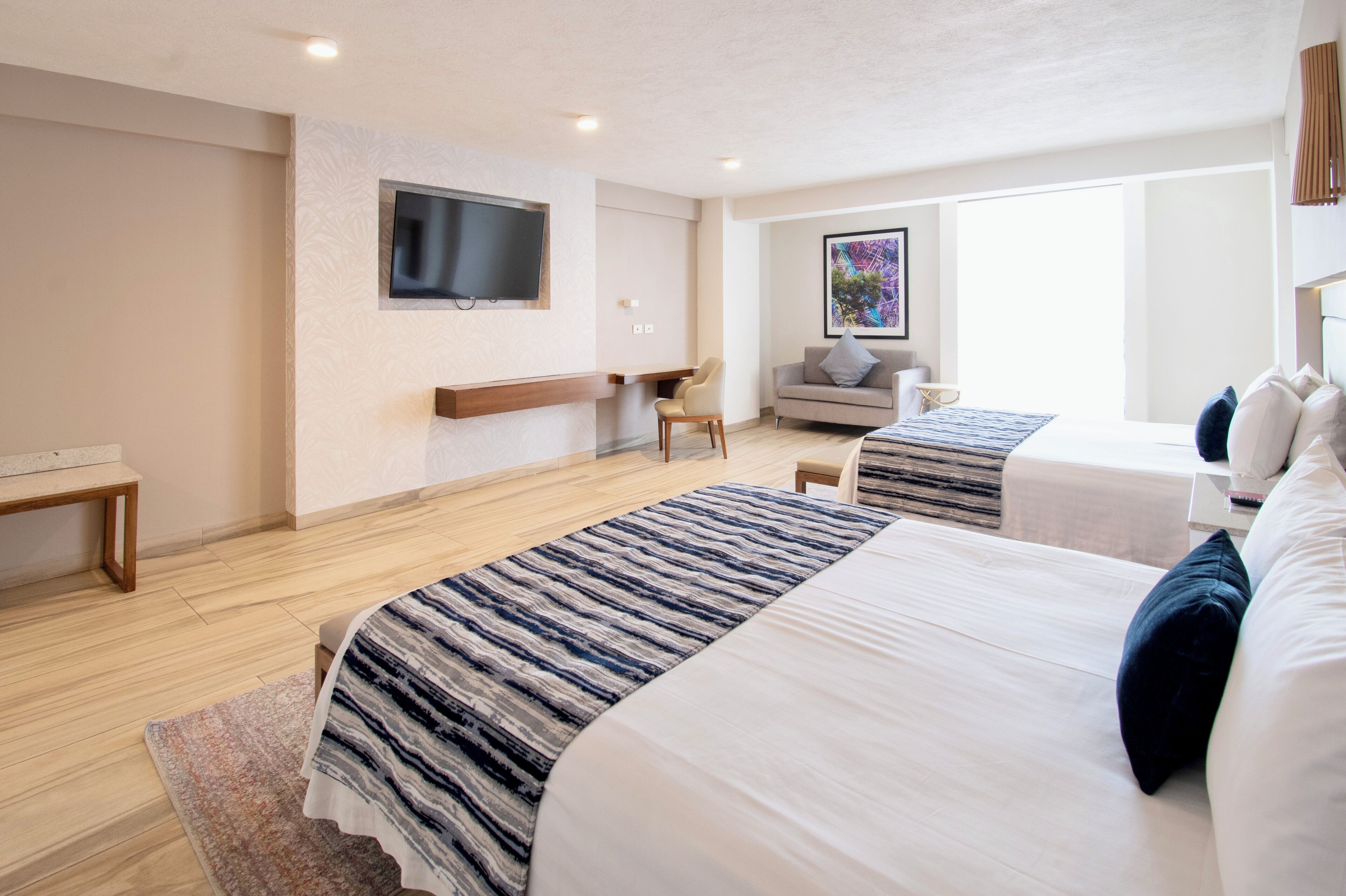 A hotel room with two beds, a TV, a sofa, and a painting.