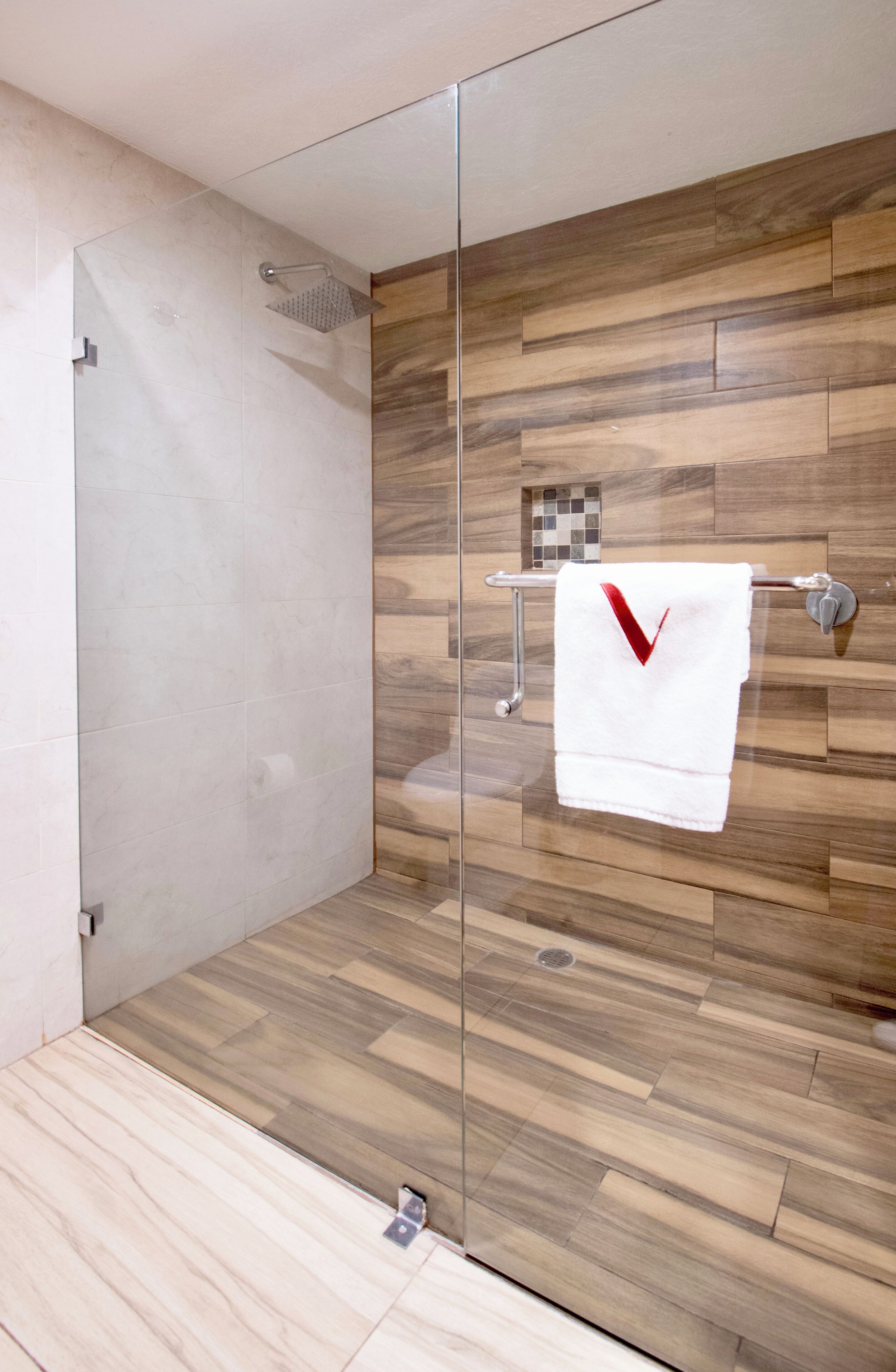 A modern bathroom with a glass shower enclosure, wooden flooring, and a towel rack with a white towel.