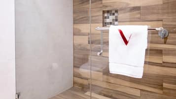 A modern bathroom with a glass shower enclosure, wooden flooring, and a towel rack with a white towel.