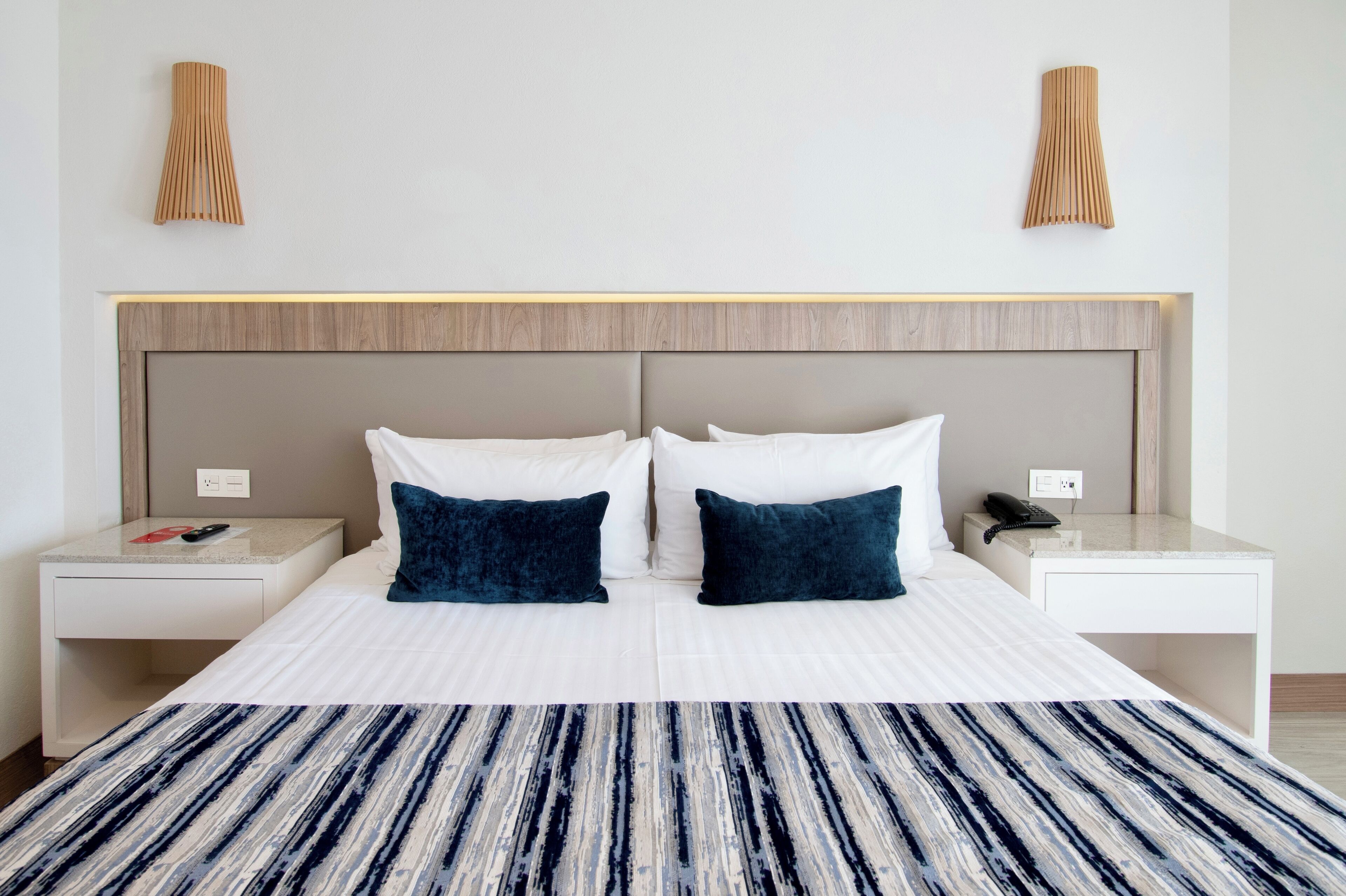 Una habitación de hotel con una cama grande, dos mesitas de noche, un cabecero y dos lámparas de pared.