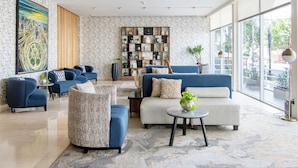 A modern living room with a large painting, a built-in bookshelf, and a view through large windows. - Hotel Velvet Plaza (Guadalajara)