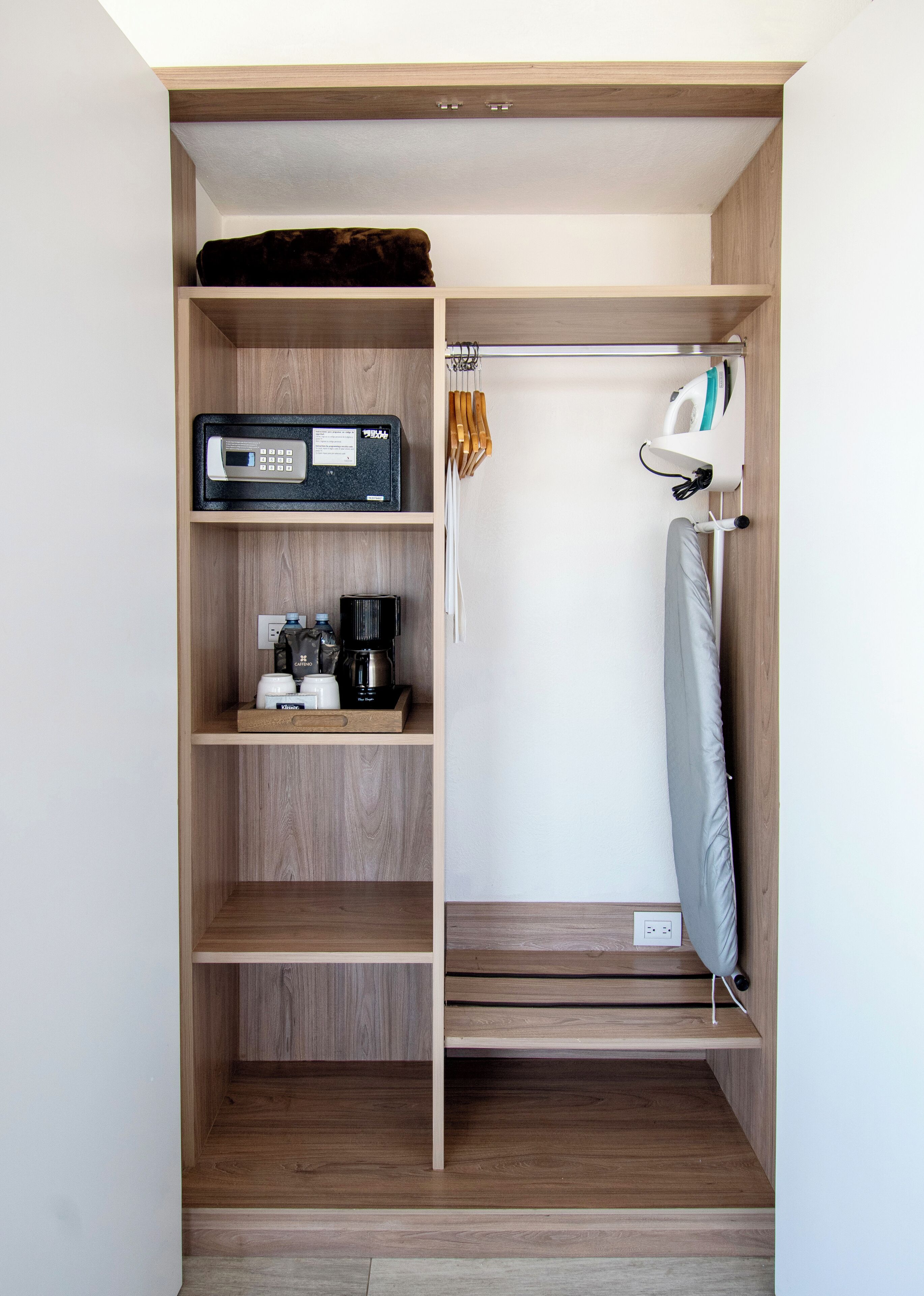 A compact, well-organized closet with wooden shelves, a hanging rack, and a foldable ironing board.