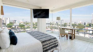 A modern hotel room with a large bed, a desk, and a TV. The room has large windows offering a city view. - Hotel Velvet Plaza (Guadalajara)