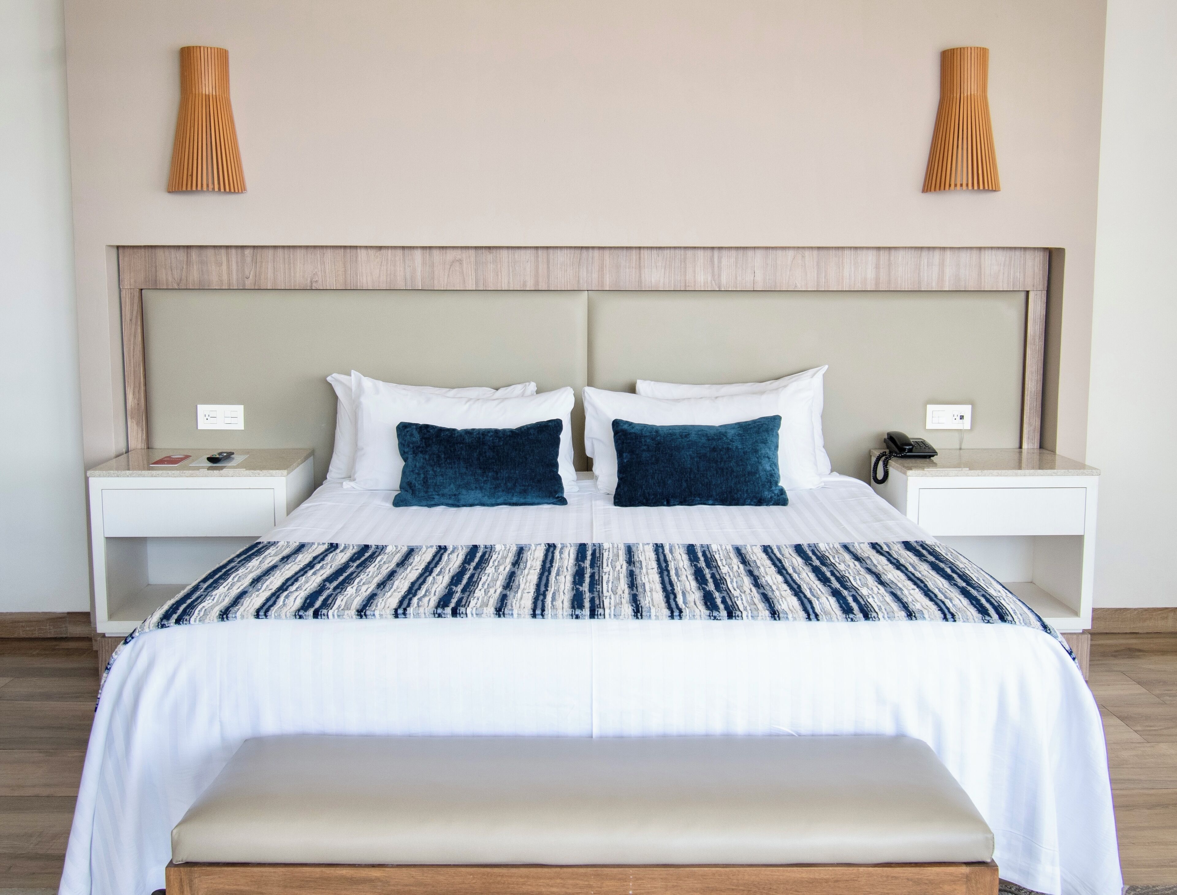 A hotel room with a large bed, two bedside tables, a bedside lamp, and a wooden bench.