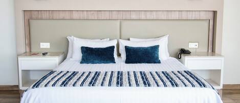 A hotel room with a large bed, two bedside tables, a bedside lamp, and a wooden bench.