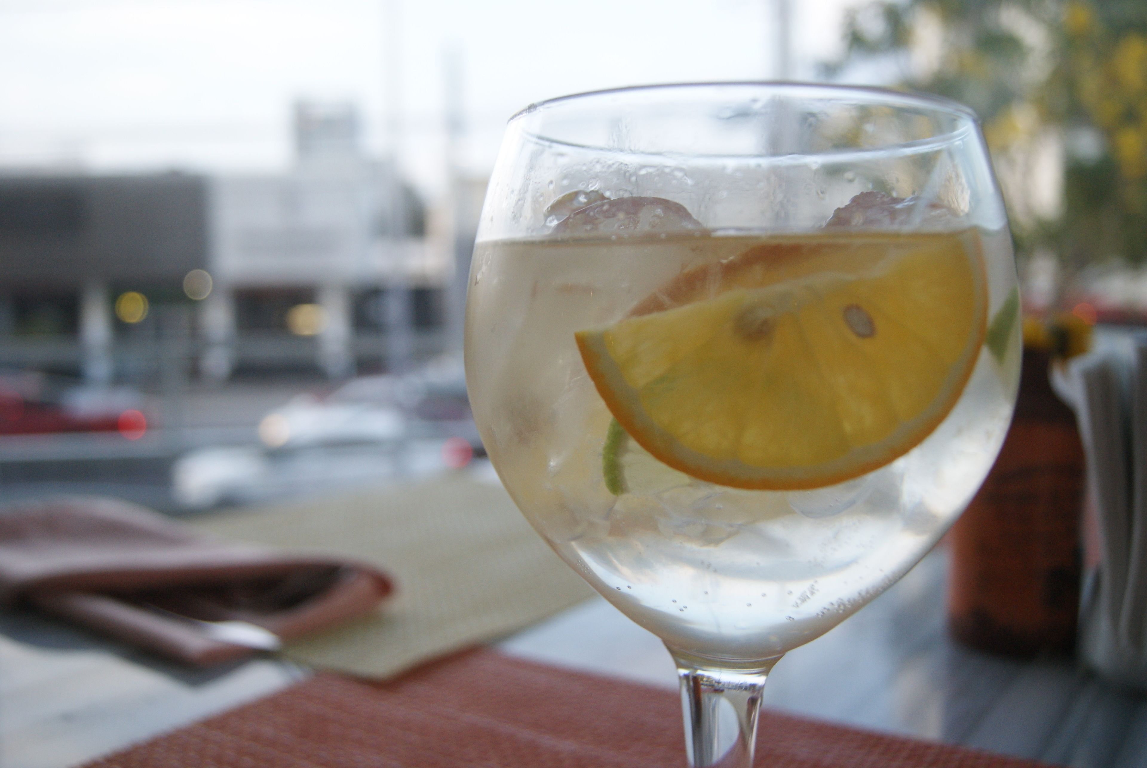 A glass of water with an orange slice on a table with a red napkin and a brown bag.