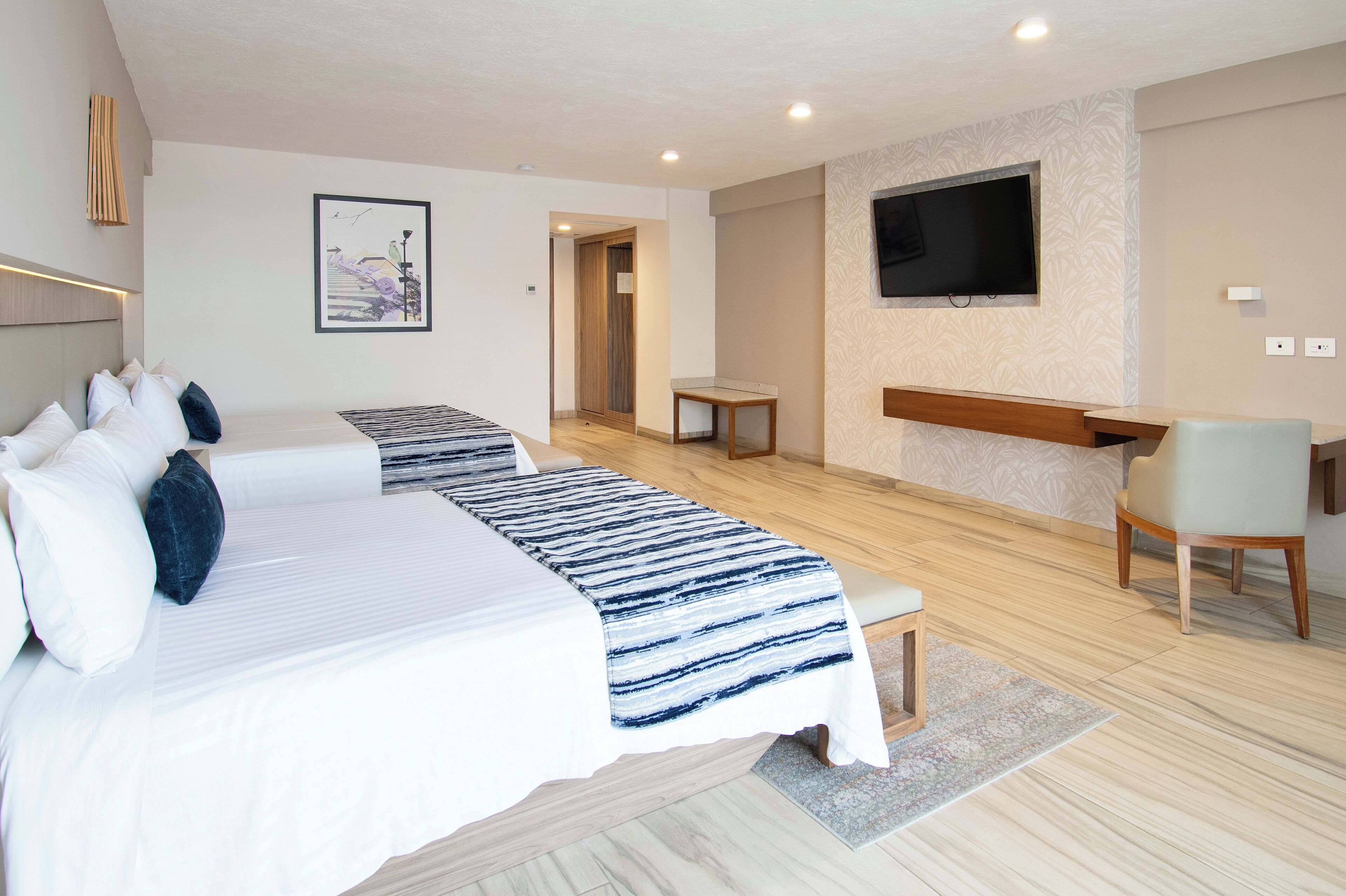 A hotel room with two beds, a TV mounted on the wall, a desk, and a chair.