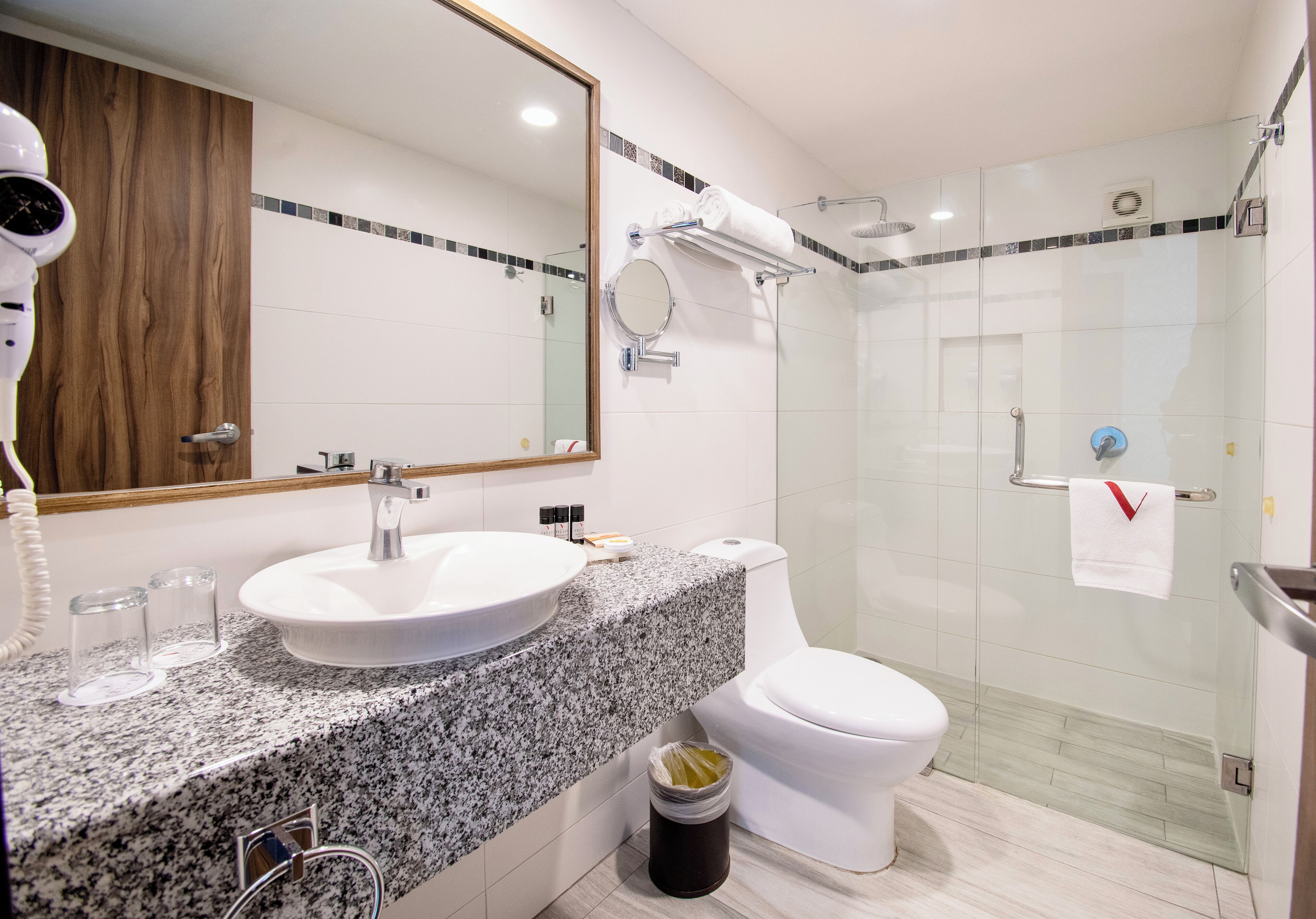 Un baño moderno con encimera de granito, un lavamanos blanco, inodoro y ducha con mampara de cristal.