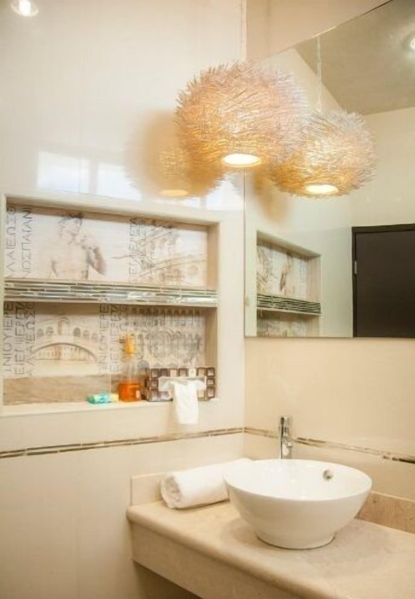 Un baño con lavamanos blanco, un espejo y un aplique decorativo en el techo.