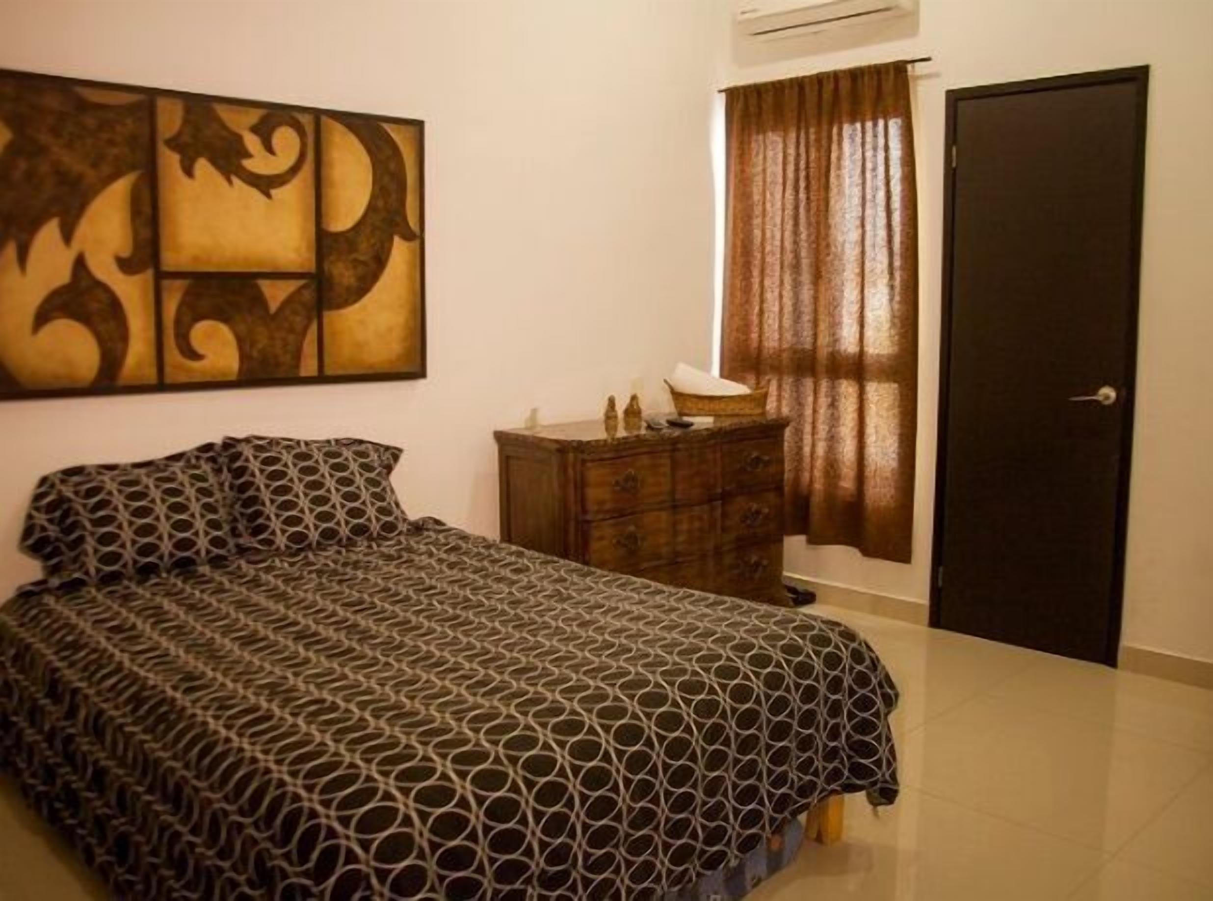 A bedroom with a bed, a dresser, a door, and a wall with a decorative piece.