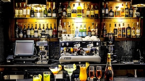A bar area with multiple shelves of liquor bottles, a bar counter with glasses and a bottle of champagne, and a coffee machine. - Magna Hotel and Suites (Nairobi)