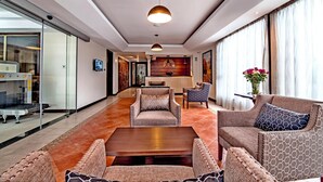A spacious lobby with a reception desk, seating area with sofas and armchairs, and a large window with curtains. - Magna Hotel and Suites (Nairobi)