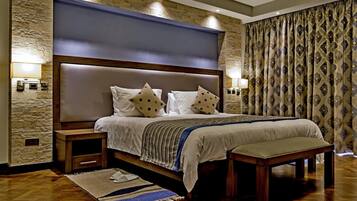 Un dormitorio con una cama grande, mesitas de noche de madera, un banco, una pared de piedra y cortinas estampadas.