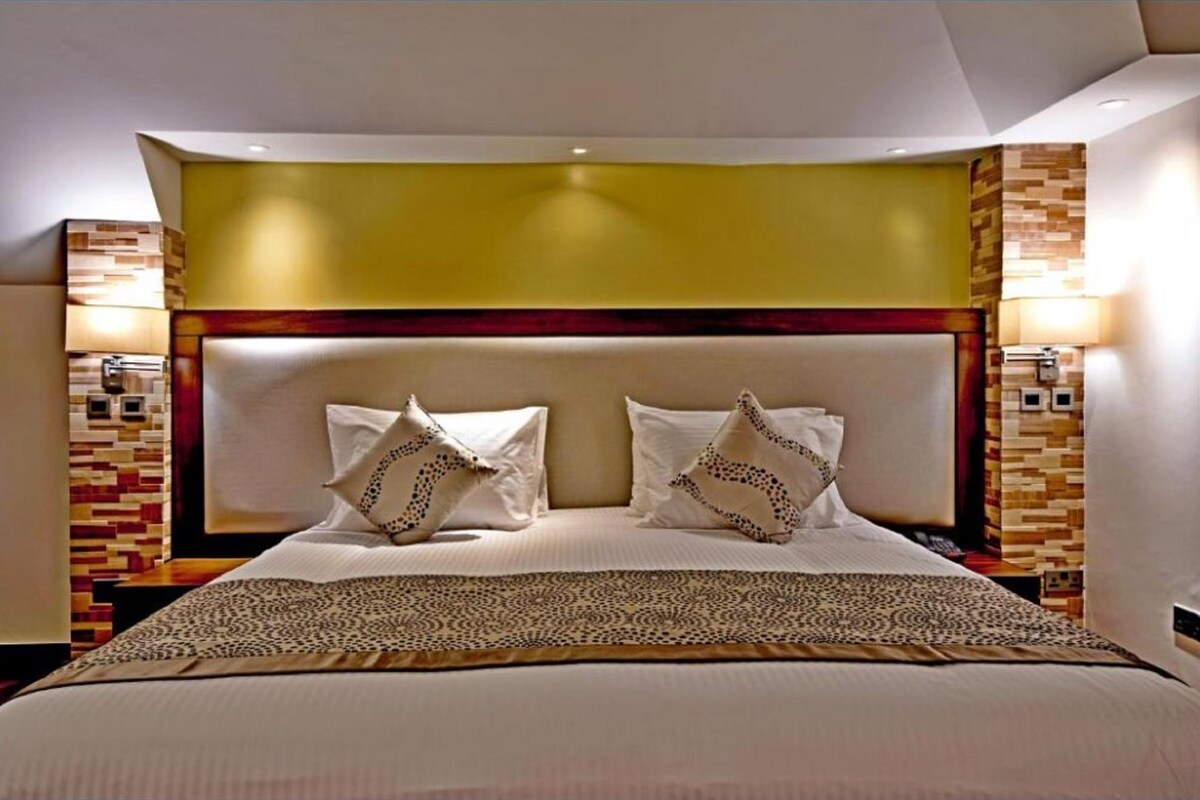 Ein Hotelzimmer mit einem großen Bett, zwei Nachttischlampen, einem Kopfteil mit geometrischem Muster und einer gemusterten Tagesdecke.
