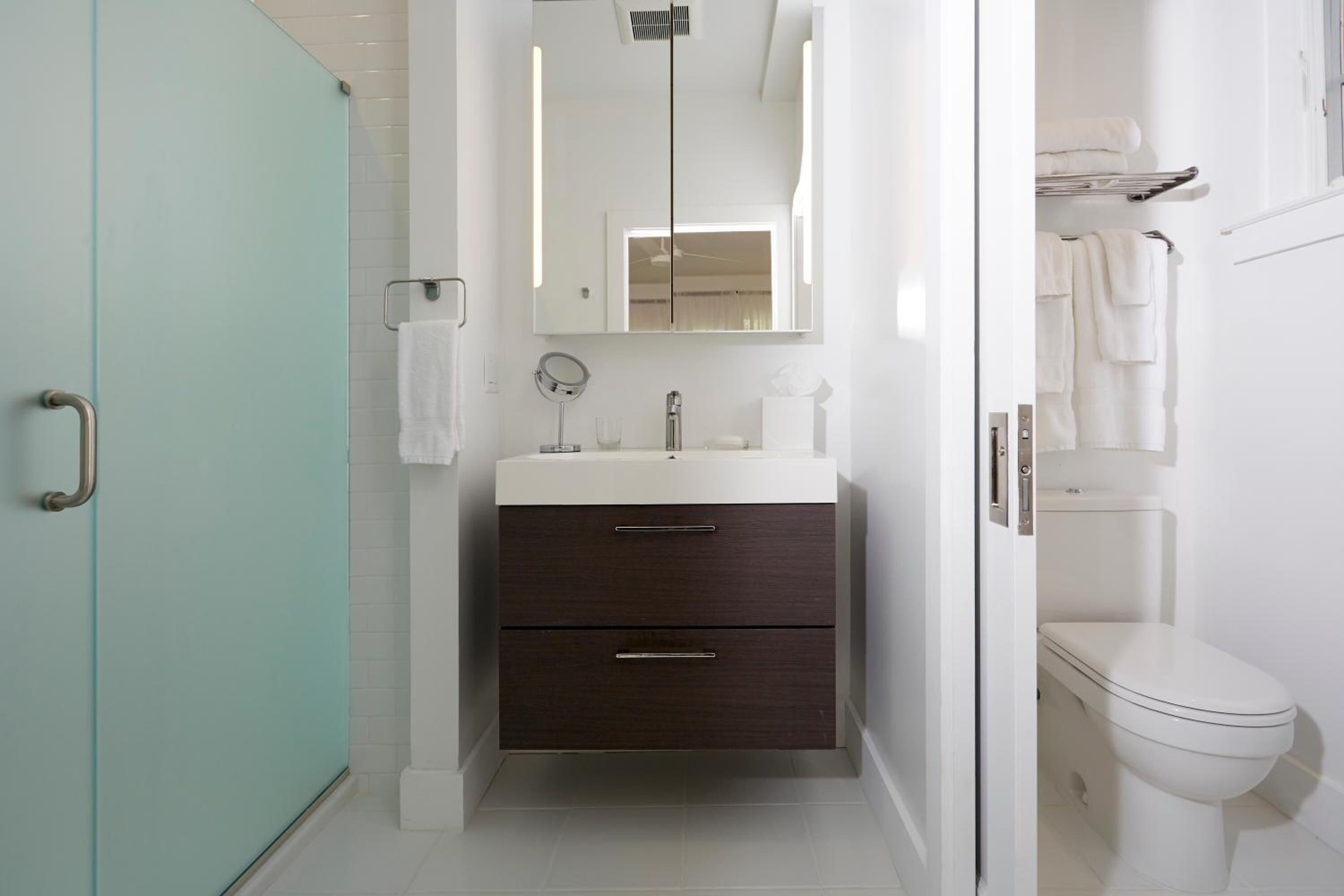 A modern bathroom with a glass shower enclosure, a white sink with a dark cabinet, and a white toilet.