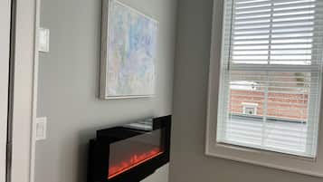 A modern living room with a fireplace, a window with blinds, and a piece of abstract art on the wall.