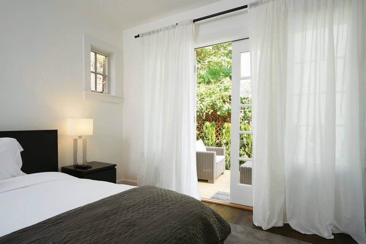 A bedroom with a bed, a nightstand, a lamp, and a view of an outdoor patio with wicker furniture.