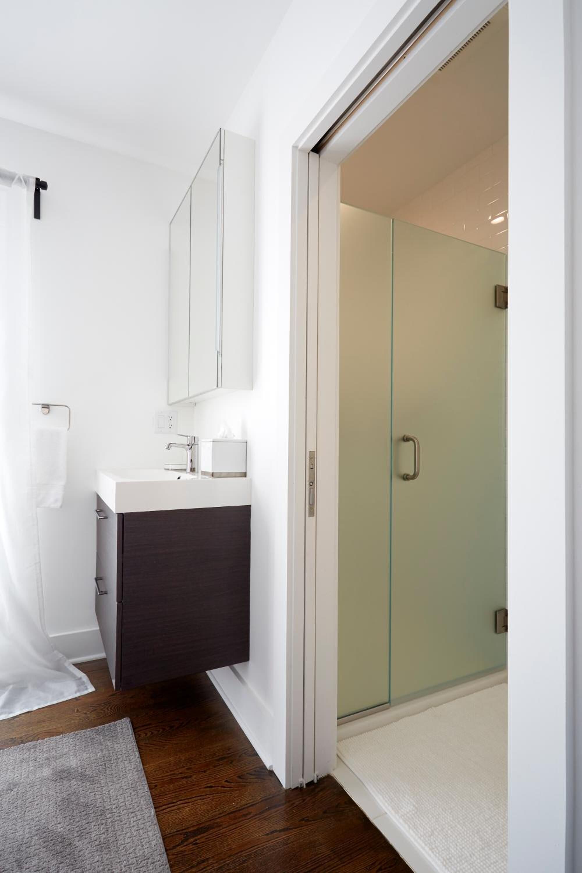 Une salle de bain moderne avec une douche à l’italienne en verre, un lavabo blanc avec un meuble sombre en dessous, et un miroir au-dessus du lavabo.