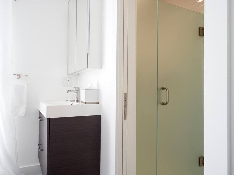 Une salle de bain moderne avec une douche à l’italienne en verre, un lavabo blanc avec un meuble sombre en dessous, et un miroir au-dessus du lavabo.