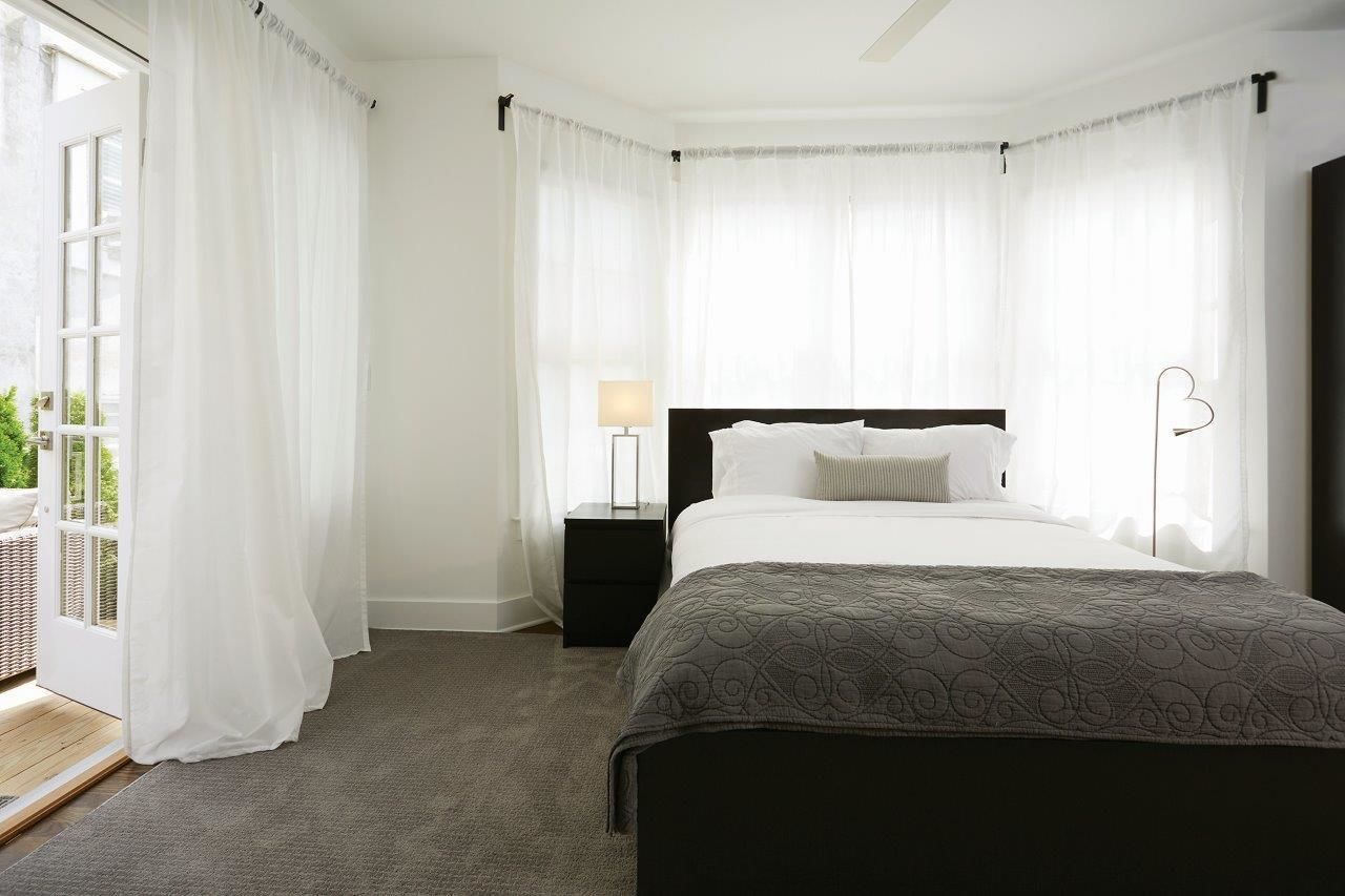 Une chambre à coucher avec un lit, des tables de chevet, une lampe et des rideaux légers.
