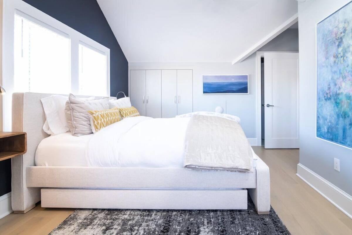 A bedroom with a bed, a nightstand, a window, a door, and a painting on the wall.