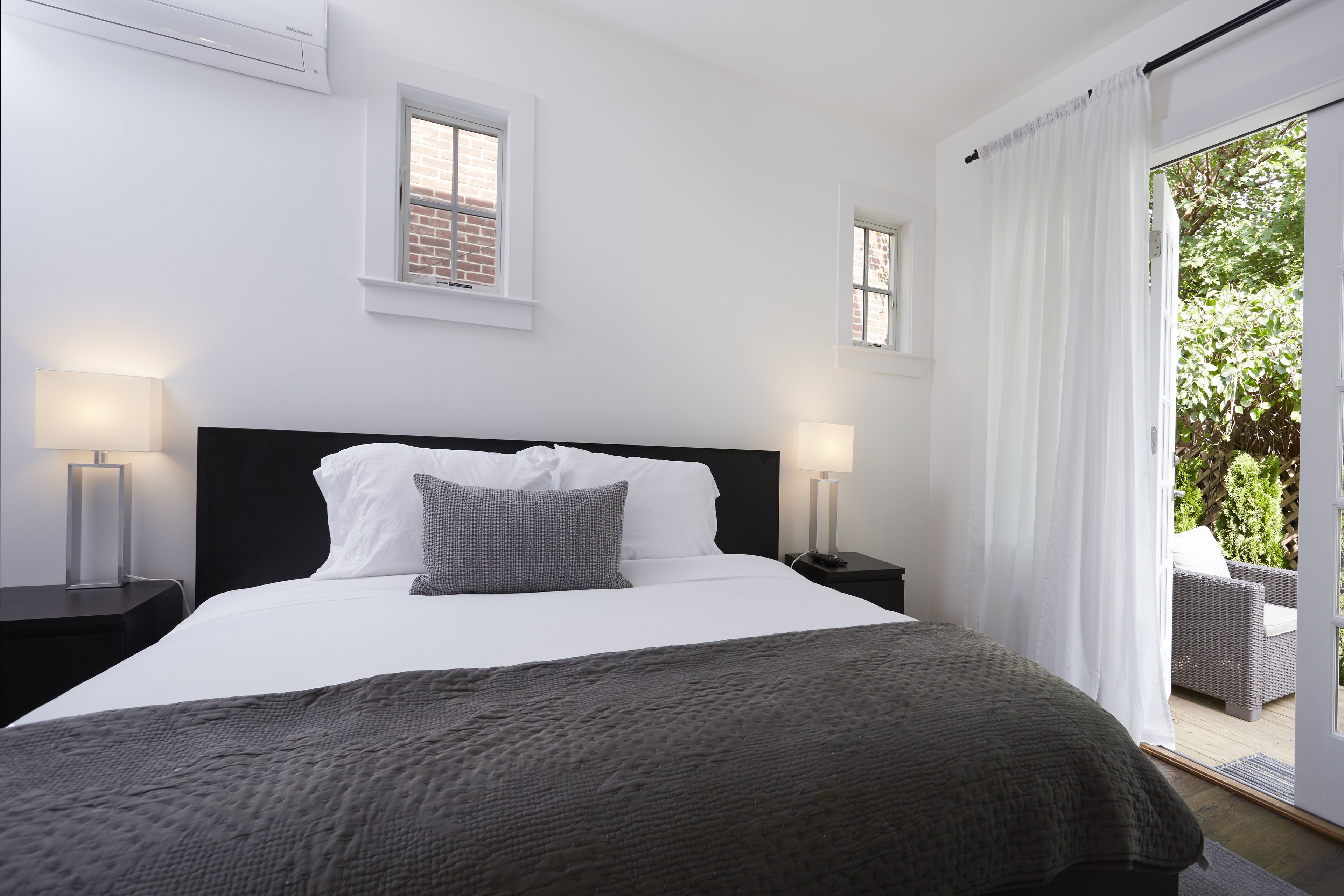 Camera d'albergo moderna con un letto grande, due comodini con lampade, vista sull'esterno tramite una porta scorrevole in vetro e un muro in mattoni visibile da una finestra.