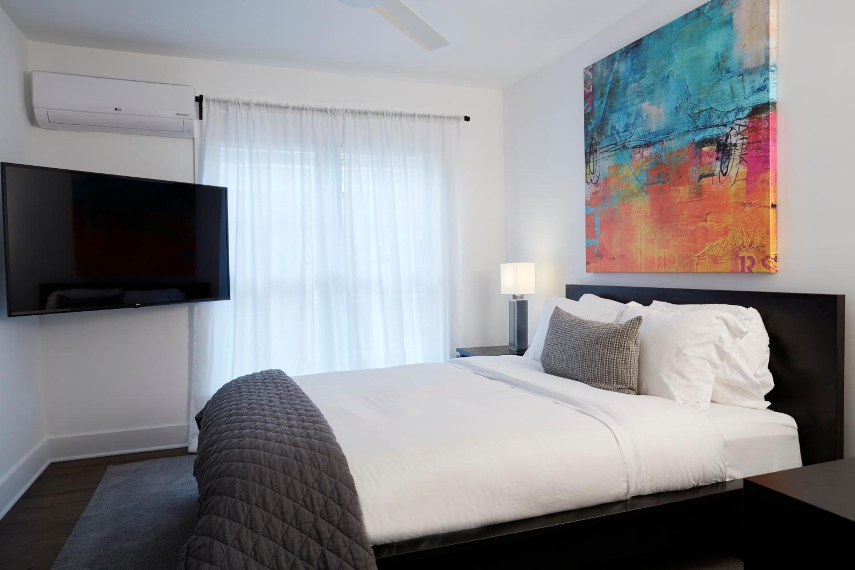 Habitación de hotel moderna con una cama grande, un televisor de pantalla plana en la pared, un ventilador de techo y un cuadro abstracto y colorido en la pared.