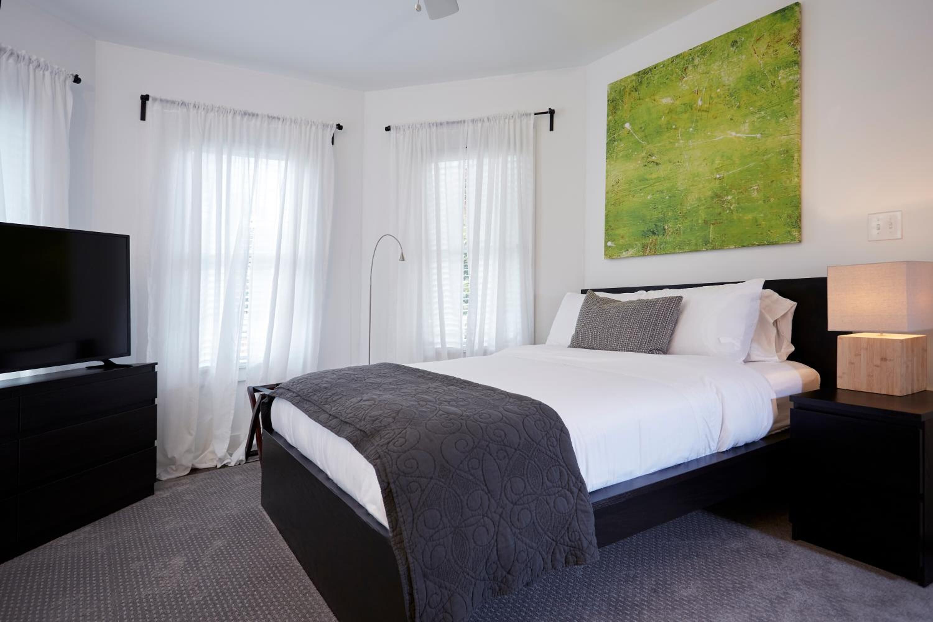 Une chambre d’hôtel moderne avec un grand lit, un téléviseur à écran plat, une table de chevet et un tableau au mur.