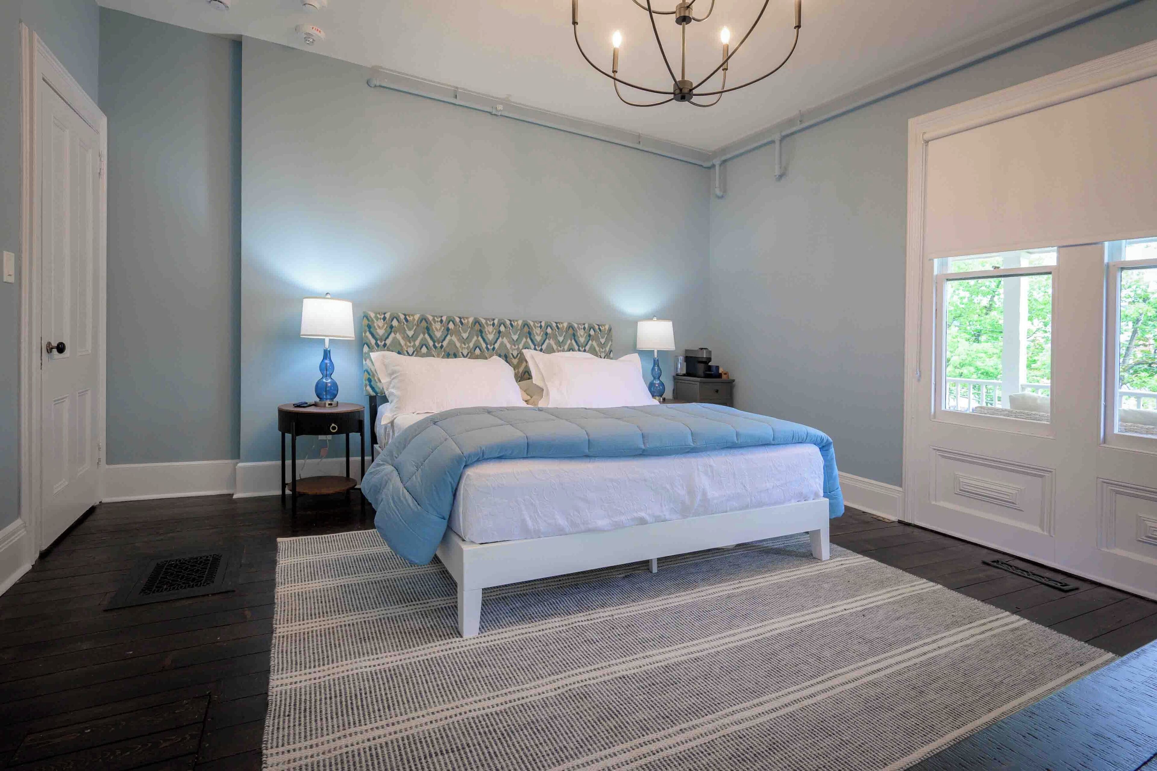 A bedroom with a bed, two bedside tables, a chandelier, and a window.