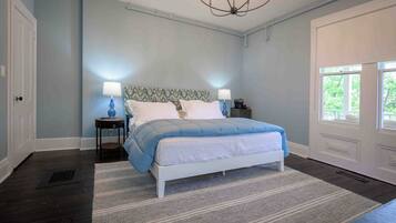 A bedroom with a bed, two bedside tables, a chandelier, and a window.