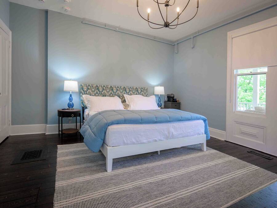A bedroom with a bed, two bedside tables, a chandelier, and a window.