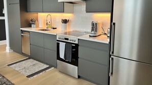 A modern kitchen with grey cabinetry, a stainless steel refrigerator, a built-in oven, and a coffee maker. - Station Inn Pawling (Pawling)