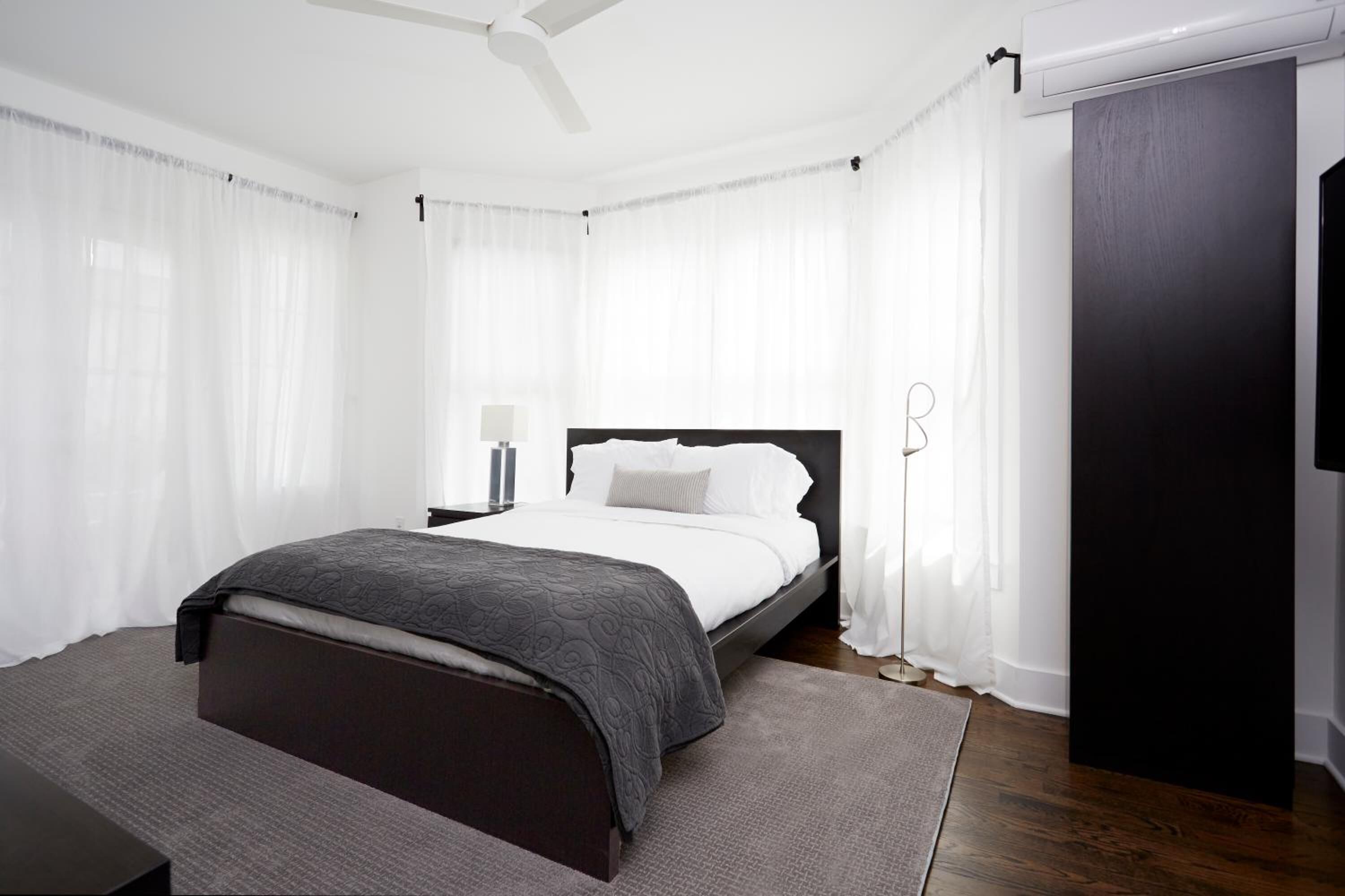 A modern bedroom with a large bed, a bedside table, a floor lamp, and a dark wooden wardrobe.