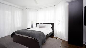 A modern bedroom with a large bed, a bedside table, a floor lamp, and a dark wooden wardrobe.