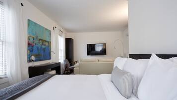 A hotel room with a large bed, a desk with a chair, a TV mounted on the wall, and a painting on the wall.