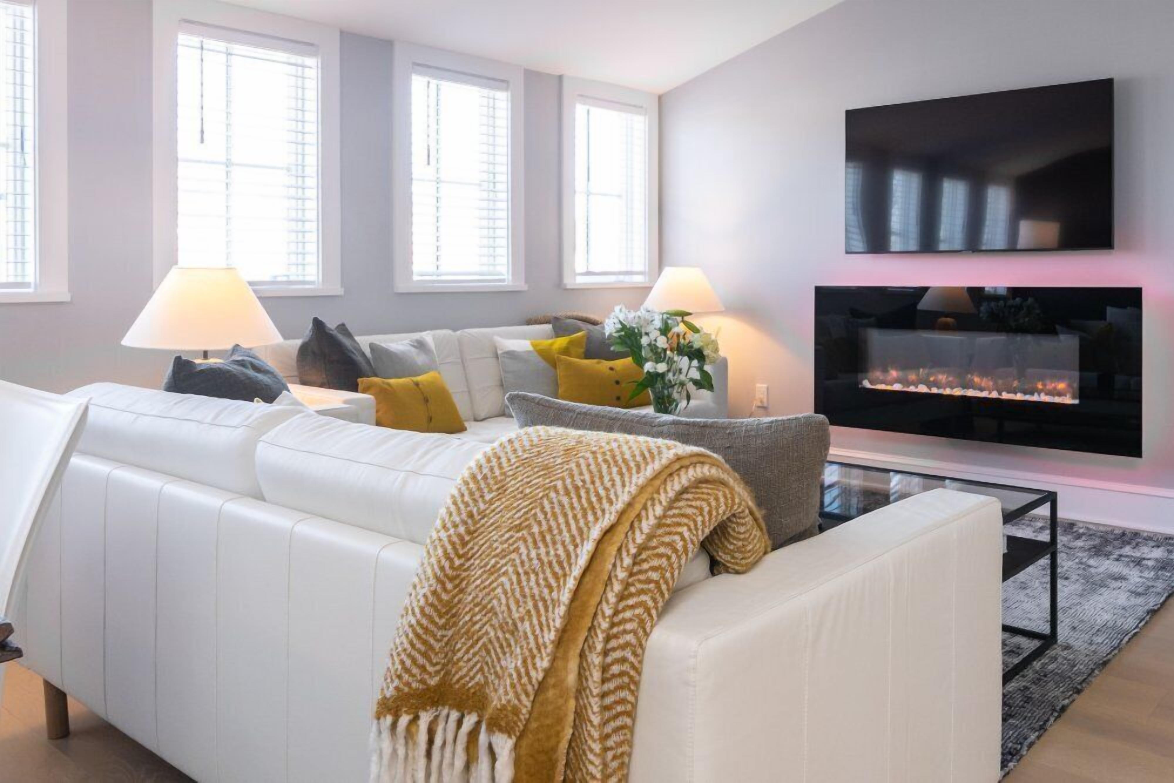 Una sala de estar moderna con un sofá blanco, dos lámparas, una chimenea y un televisor montado en la pared.