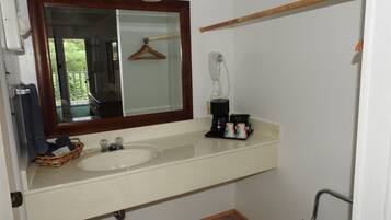 Un baño con lavamanos doble, un espejo con luces, un perchero para toallas, un perchero para abrigos, una cafetera y una silla para la ducha.