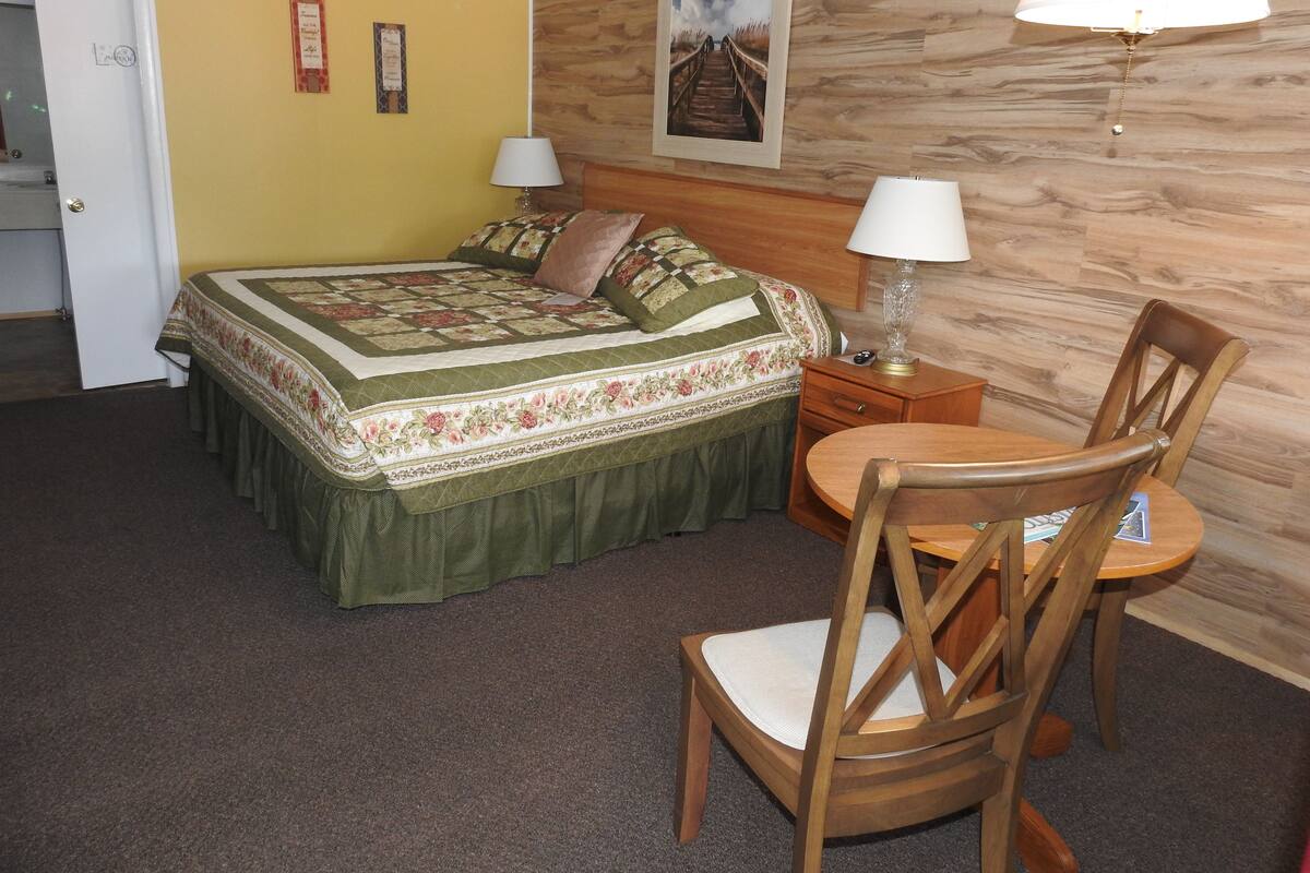 A bedroom with a bed, a nightstand, a chair, and a lamp.