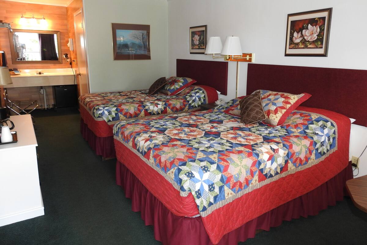 A hotel room with two beds, a desk, a chair, and a small kitchenette.