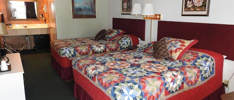 A hotel room with two beds, a desk, a chair, and a small kitchenette.