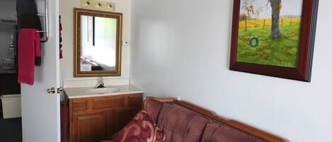 Una habitación con un tocador de madera, un espejo, un cuadro enmarcado de un árbol y un sofá marrón con cojines estampados.