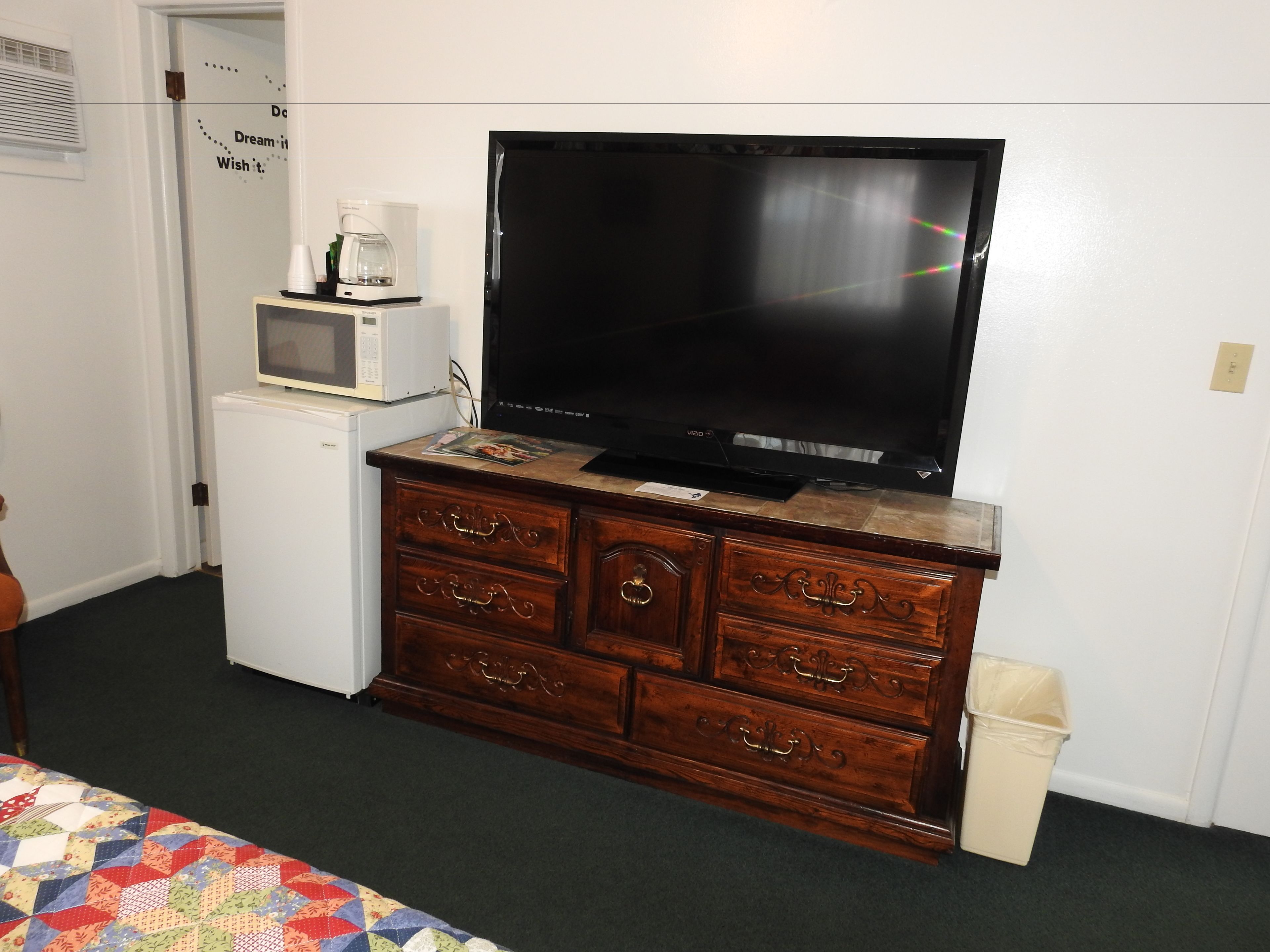 A bedroom with a wooden dresser, a television, a microwave, and a small refrigerator.