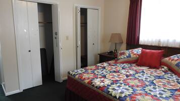 Quarto com cama grande, dois armários abertos, mesa de cabeceira com abajur e janela com cortinas.