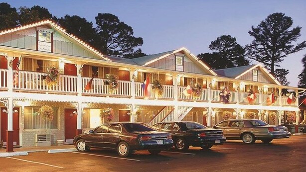 A two-story motel with a balcony on each floor, a parking lot, and a storefront with a sign.