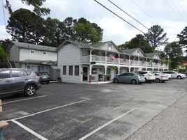 Un motel con una estructura de dos pisos, un estacionamiento y varios coches aparcados al frente.