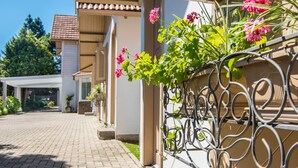 En asfalteret indkørsel fører til et hus med hegn og blomstrende planter.